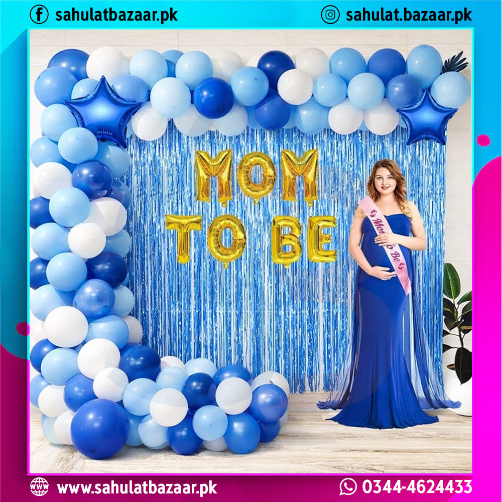 Decorative setup with balloons and 'Mom to Be' sign, featuring a woman in a blue dress.